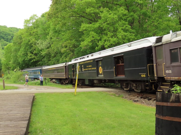 A vintage train parked near a green landscape, with two people walking alongside the tracks.