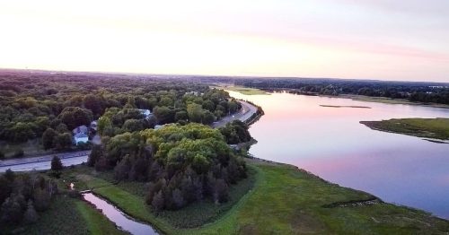 Aerial view of a serene river winding through lush greenery at sunset, with soft pastel colors in the sky.