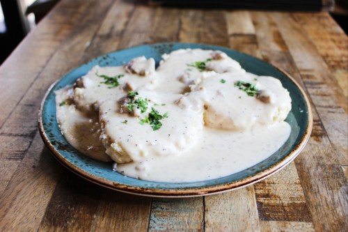 A plate of biscuits smothered in creamy sausage gravy, garnished with parsley, on a wooden table.