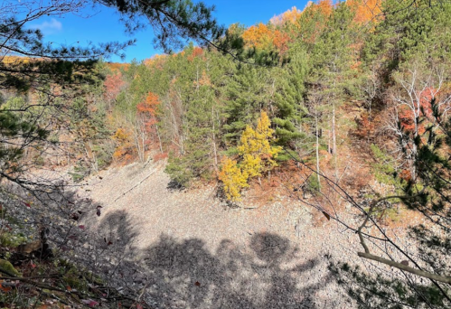 A scenic view of a rocky landscape surrounded by trees with vibrant autumn foliage under a clear blue sky.