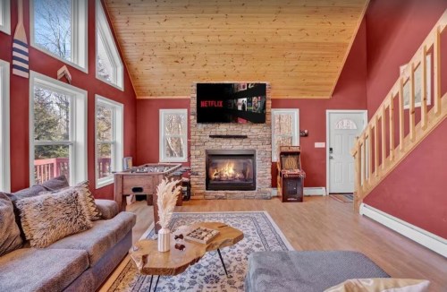 Cozy living room with a stone fireplace, large windows, and a TV mounted on the wall, featuring a warm, inviting atmosphere.