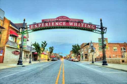 A street view of downtown Whiting, featuring an archway sign that reads "Experience Whiting" and shops lining the road.