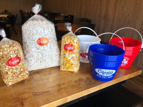 Bags of popcorn in various flavors and colorful buckets on a wooden table in a cozy setting.