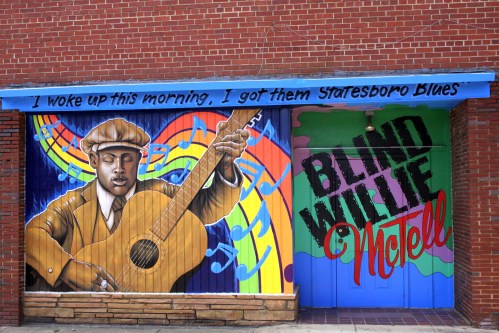 A vibrant mural featuring a musician playing guitar, with musical notes and the text "Blind Willie McTell."