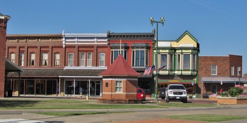 Historic buildings line a street, showcasing colorful facades and a small gazebo in a sunny town square.