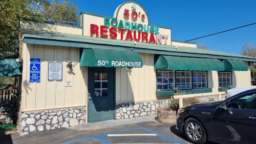 A retro-style restaurant building with a sign reading "50's Roadhouse" and green awnings, set against a clear blue sky.