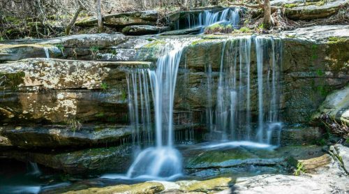 A serene waterfall cascading over rocky terrain, surrounded by lush greenery and natural beauty.