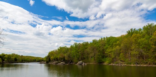 A serene lake surrounded by lush green trees under a partly cloudy sky.
