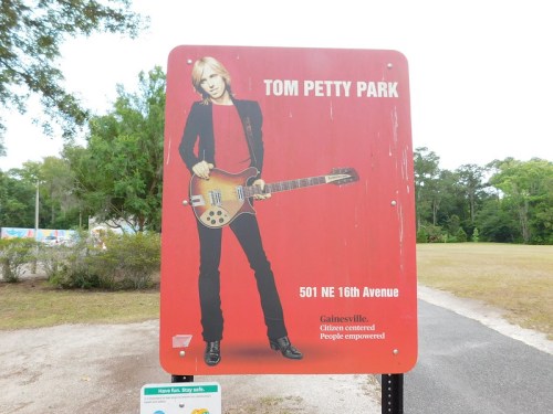 Sign for Tom Petty Park featuring a red background and an image of a musician with a guitar. Location: 501 NE 16th Avenue.