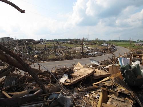 A devastated landscape with debris and destruction along a winding road, under a cloudy sky.