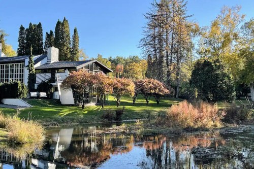 A serene landscape featuring a pond, colorful trees, and a modern building surrounded by lush greenery in autumn.