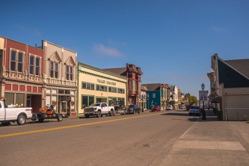 A quiet street lined with colorful historic buildings and parked cars under a clear blue sky.