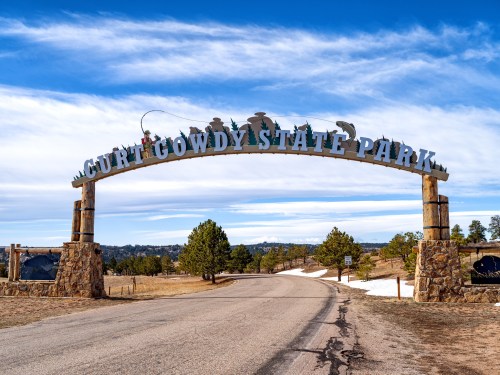 Archway sign for Curt Gowdy State Park, with a clear blue sky and a road leading into the park.