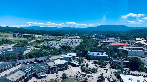 A panoramic view of a town with shops, parking lots, and mountains under a clear blue sky.