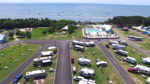 Aerial view of a campground with RVs, a pool, and a beach in the background under a clear blue sky.