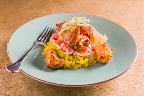 A plate of vibrant yellow rice topped with lobster, meat, and garnished with shredded cabbage, served with fried pieces.