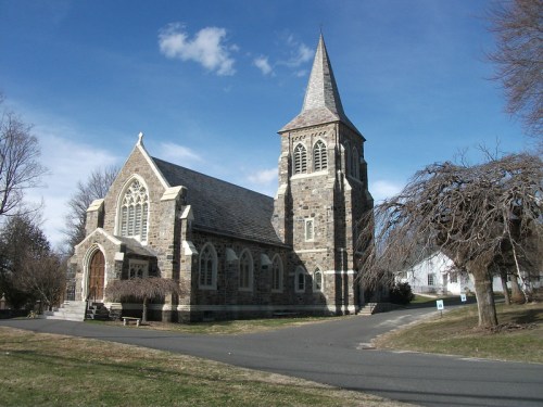 A stone church with a tall steeple, surrounded by trees and a clear blue sky.