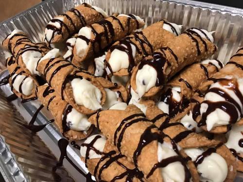 A tray of cannoli filled with creamy filling and drizzled with chocolate sauce.