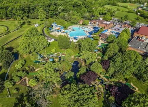 Aerial view of a recreational area featuring a pool, water slides, mini-golf, and lush green landscaping.