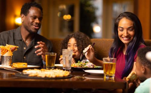 A family enjoys a meal together at a restaurant, smiling and sharing food and drinks.
