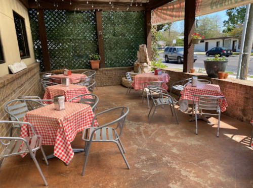 Outdoor dining area with checkered tablecloths, metal chairs, and greenery in the background. Bright and inviting atmosphere.