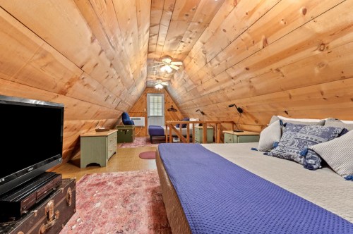 Cozy attic bedroom with wooden walls, a bed, TV, and rustic decor, featuring a warm, inviting atmosphere.