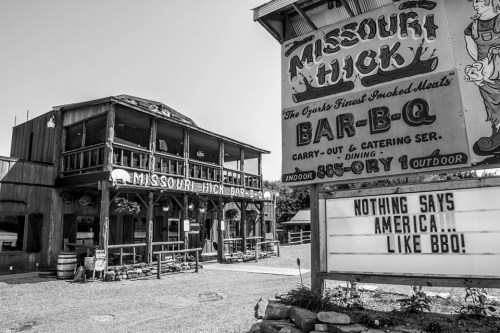 Black and white photo of a rustic BBQ restaurant with a sign reading "Nothing says America... like BBQ!"