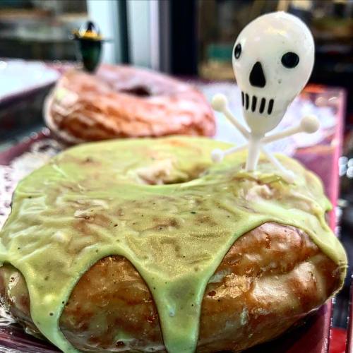 A donut topped with green icing and a small skull decoration, resembling a spooky treat.