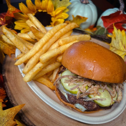 A delicious burger with pickles and crispy onions, served with golden fries, surrounded by autumn leaves and decor.