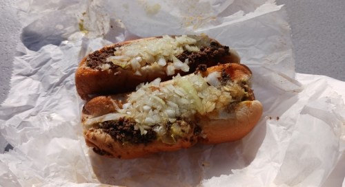 Two hot dogs topped with chopped onions, resting on crumpled white paper.