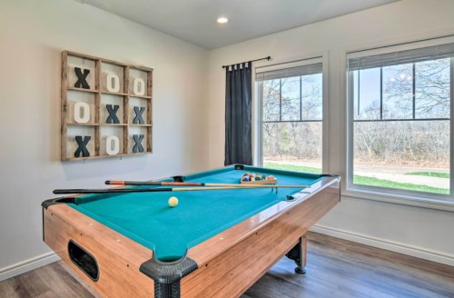 A pool table with cues and balls, next to a window and a wall art featuring a tic-tac-toe design.