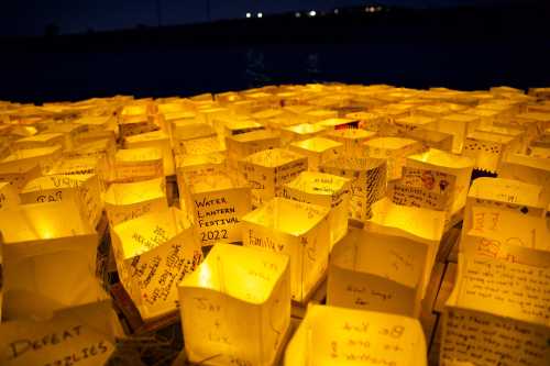 A close-up of glowing lanterns with handwritten messages, floating on water during the Water Lantern Festival 2022.