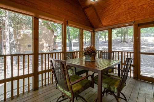 A cozy screened porch with a wooden table and chairs, surrounded by trees and natural light.