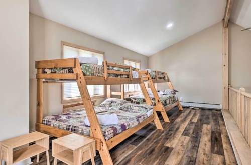 A spacious room with two wooden bunk beds, each with bedding, and wooden side tables on a hardwood floor.