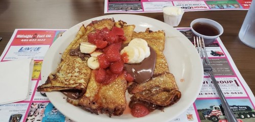 A plate of crepes filled with chocolate, topped with strawberries, banana slices, and a dollop of whipped cream.