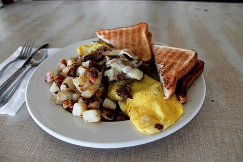 A plate of breakfast featuring an omelet, toast, and seasoned potatoes.