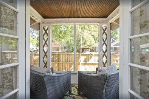 A cozy sunroom with two wicker chairs, surrounded by large windows and a view of a backyard.