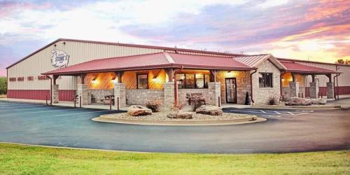 A modern building with a stone facade and red roof, surrounded by grass and rocks, under a colorful sunset sky.