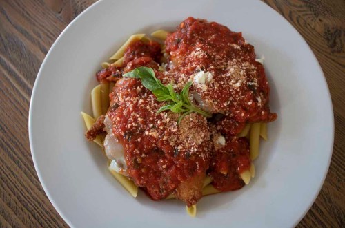 A plate of pasta topped with two pieces of breaded chicken, marinara sauce, and sprinkled with cheese and basil.
