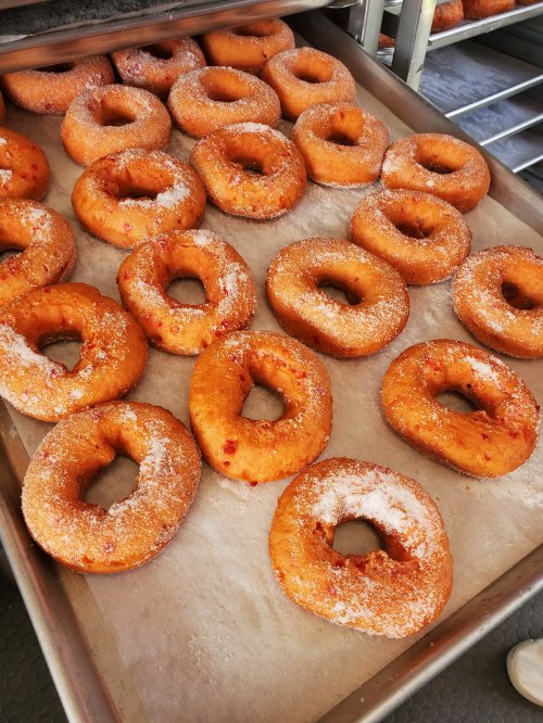 A tray of freshly made donuts coated in sugar, arranged in neat rows.