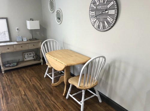 A small wooden table with two chairs in a cozy room featuring a wall clock and decorative items.