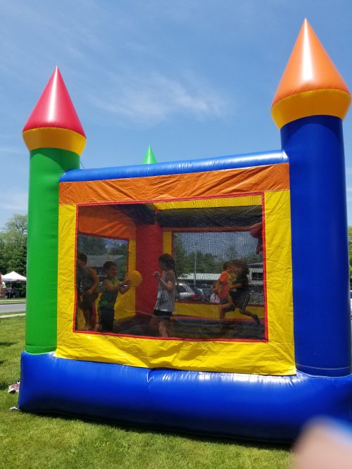 Children playing inside a colorful bounce house with tall, pointed towers on a sunny day.