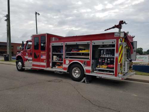 A red fire truck parked on a street, showcasing various firefighting equipment on its side compartments.