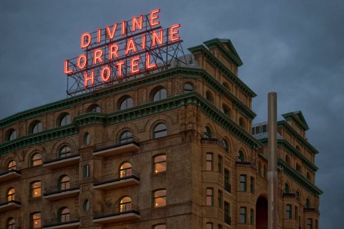 The Divine Lorraine Hotel with a glowing neon sign against a cloudy sky. Historic architecture in an urban setting.