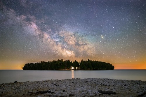A serene island under a starry night sky, with the Milky Way visible above and calm waters in the foreground.
