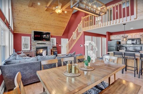 Cozy living room with a stone fireplace, wooden beams, and a dining area, featuring a modern kitchen in a warm color scheme.