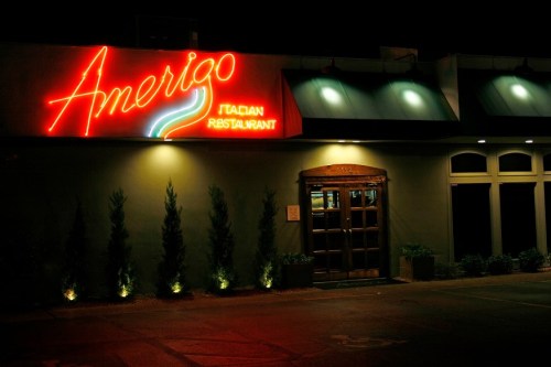 Neon sign of Amerigo Italian Restaurant illuminated at night, featuring a welcoming entrance and surrounding greenery.