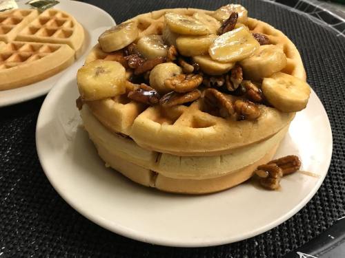 A stack of waffles topped with sliced bananas and pecans on a white plate.