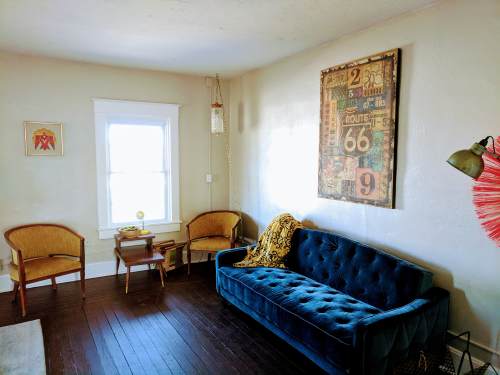 Cozy living room with a blue velvet sofa, two chairs, a small table, and vintage Route 66 artwork on the wall.