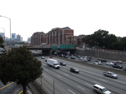 A busy highway with traffic, overpasses, and buildings in the background under a cloudy sky.